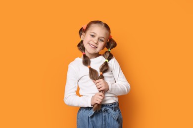 Photo of Cute little girl with beautiful hairstyle on orange background