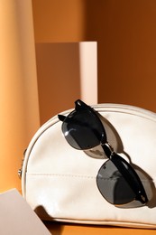 Stylish sunglasses and white makeup bag on pale orange background
