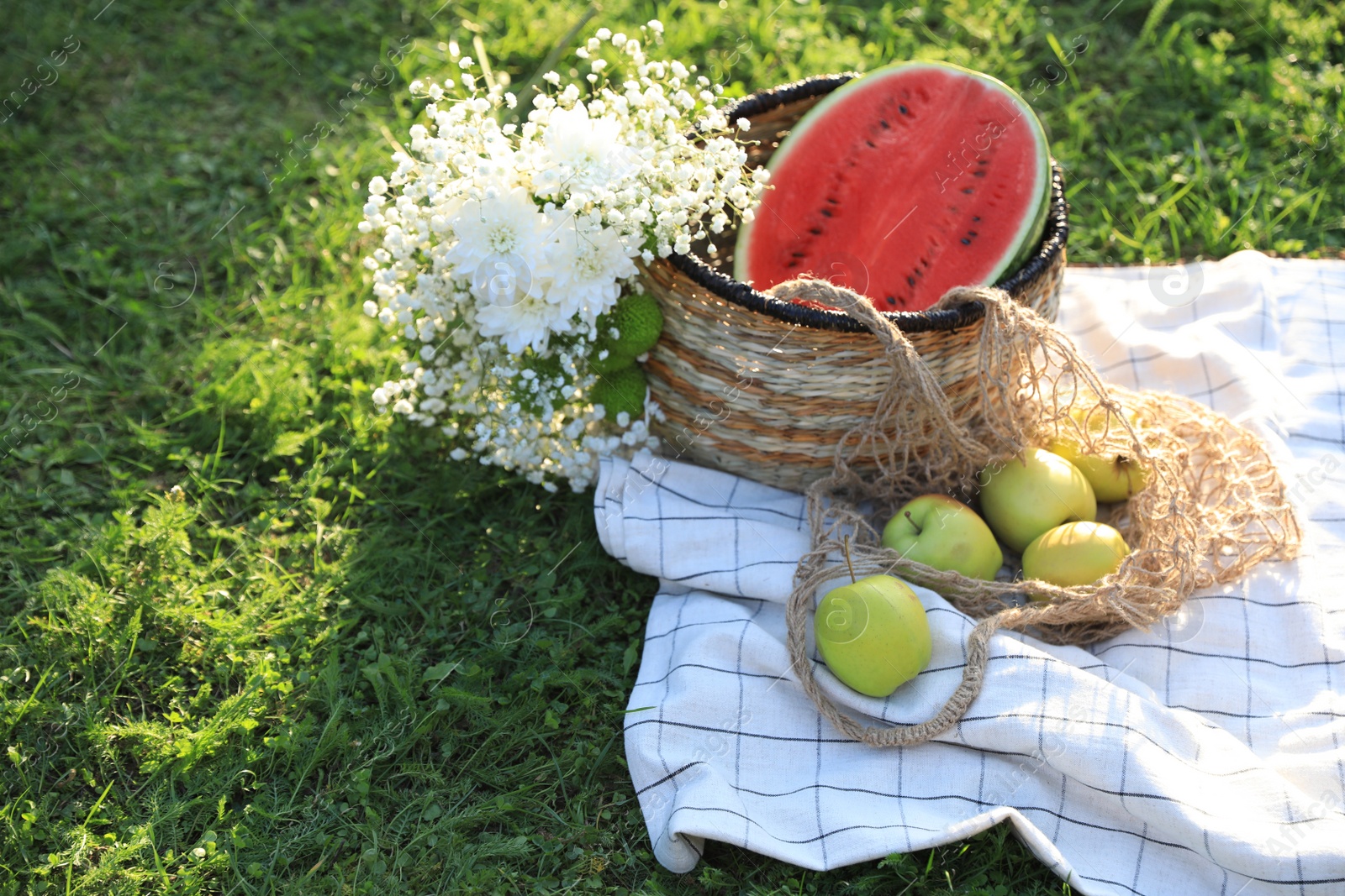 Photo of Picnic blanket with tasty fruits, beautiful flowers and basket on green grass outdoors