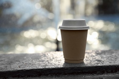 Photo of Cardboard takeaway coffee cup with lid on stone parapet near fountain outdoors, space for text