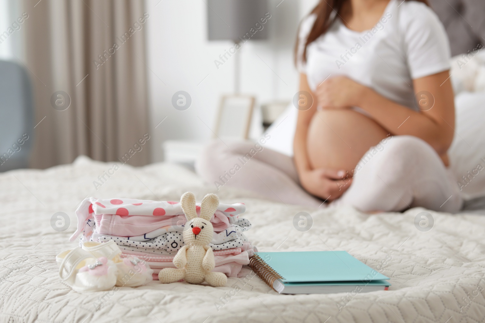 Photo of Baby clothes prepared for maternity hospital and pregnant woman on background