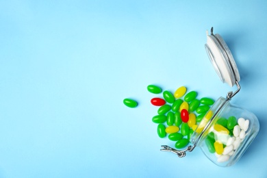 Photo of Overturned jar with jelly beans on color background, top view. Space for text