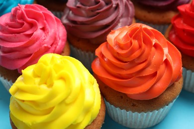 Many delicious colorful cupcakes on light blue background, closeup