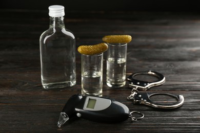 Modern breathalyzer, alcohol and handcuffs on dark wooden background