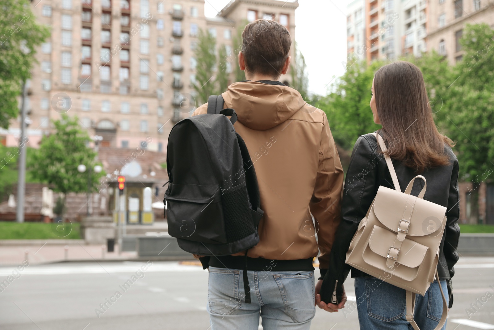 Photo of Young couple waiting to cross street, back view. Traffic rules and regulations