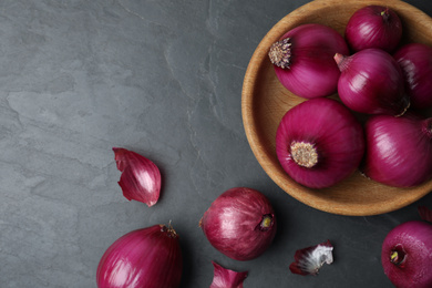Photo of Ripe red onion bulbs and bowl on black table, flat lay. Space for text