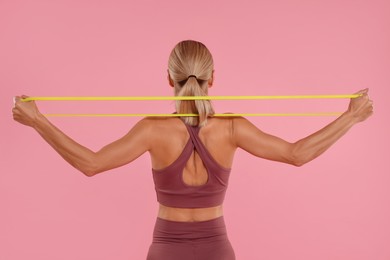 Woman exercising with elastic resistance band on pink background, back view