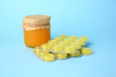 Photo of Blisters with cough drops and honey on light blue background