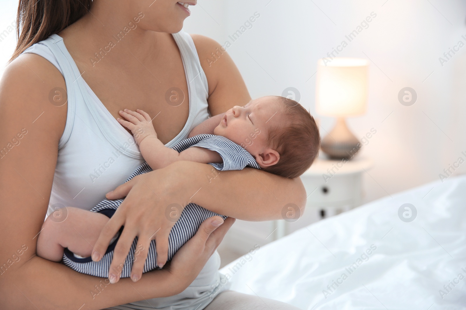 Photo of Young woman holding her baby near breast in bedroom, closeup. Space for text
