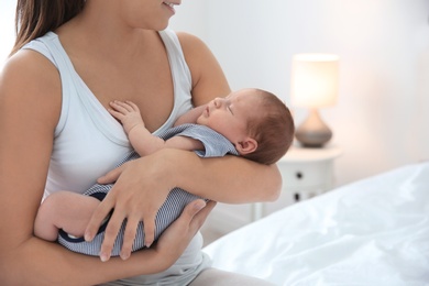 Young woman holding her baby near breast in bedroom, closeup. Space for text