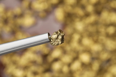 Photo of Tweezers with gold nugget on blurred background, closeup