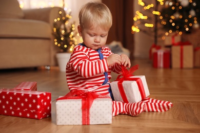 Baby in Christmas pajamas opening gift box indoors