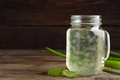 Photo of Fresh aloe drink in mason jar on wooden table. Space for text