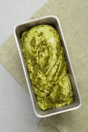 Uncooked pesto bread in baking dish on light table, top view