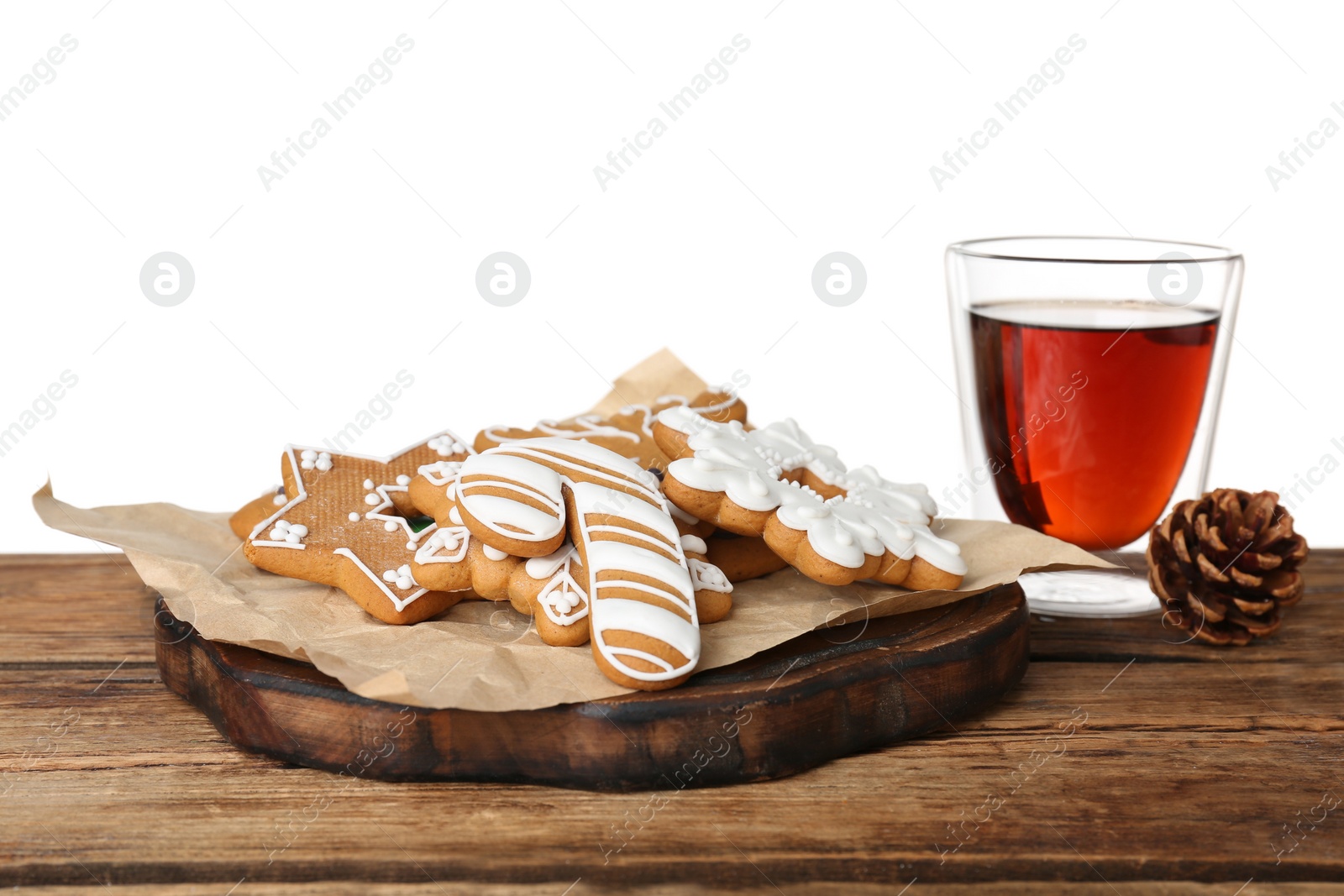 Photo of Board with tasty Christmas cookies near glass of tea on wooden table against white background