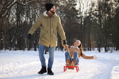 Photo of Happy young man pulling his girlfriend in sleigh outdoors on winter day