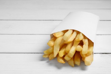 Delicious french fries in paper box on white wooden table, closeup. Space for text