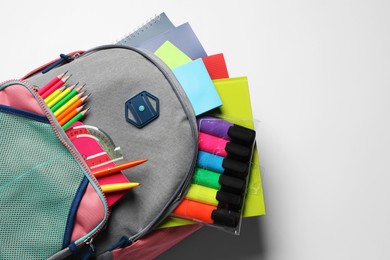 Photo of Backpack with different school stationery on white background, top view. Space for text