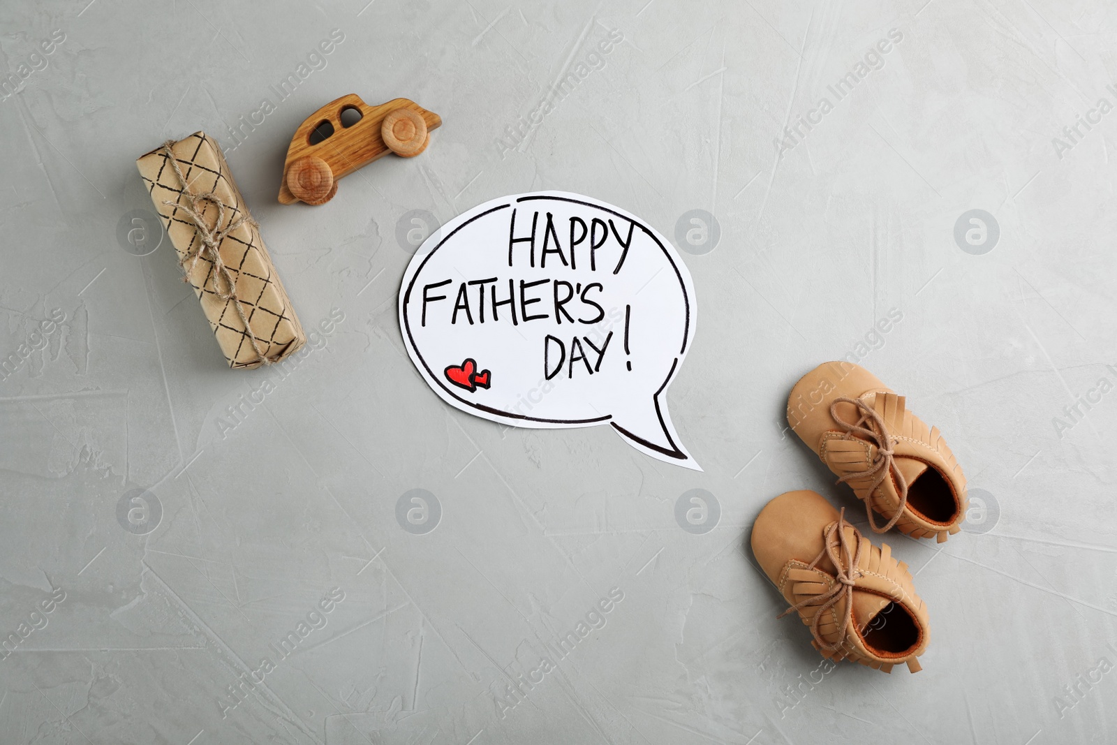 Photo of Flat lay composition with baby shoes and gift box on gray background. Happy Father's Day