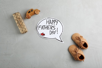 Photo of Flat lay composition with baby shoes and gift box on gray background. Happy Father's Day