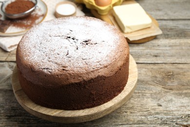 Photo of Tasty chocolate sponge cake with powdered sugar and ingredients on wooden table, closeup