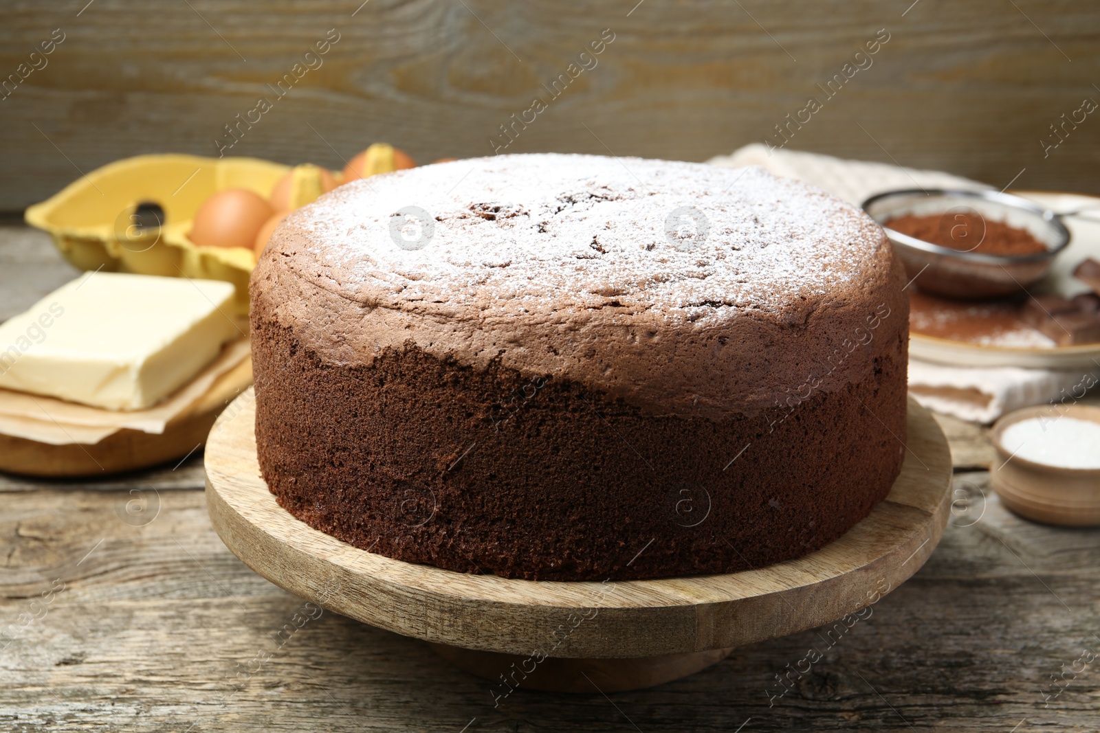 Photo of Tasty chocolate sponge cake with powdered sugar and ingredients on wooden table, closeup