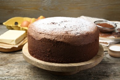 Photo of Tasty chocolate sponge cake with powdered sugar and ingredients on wooden table, closeup