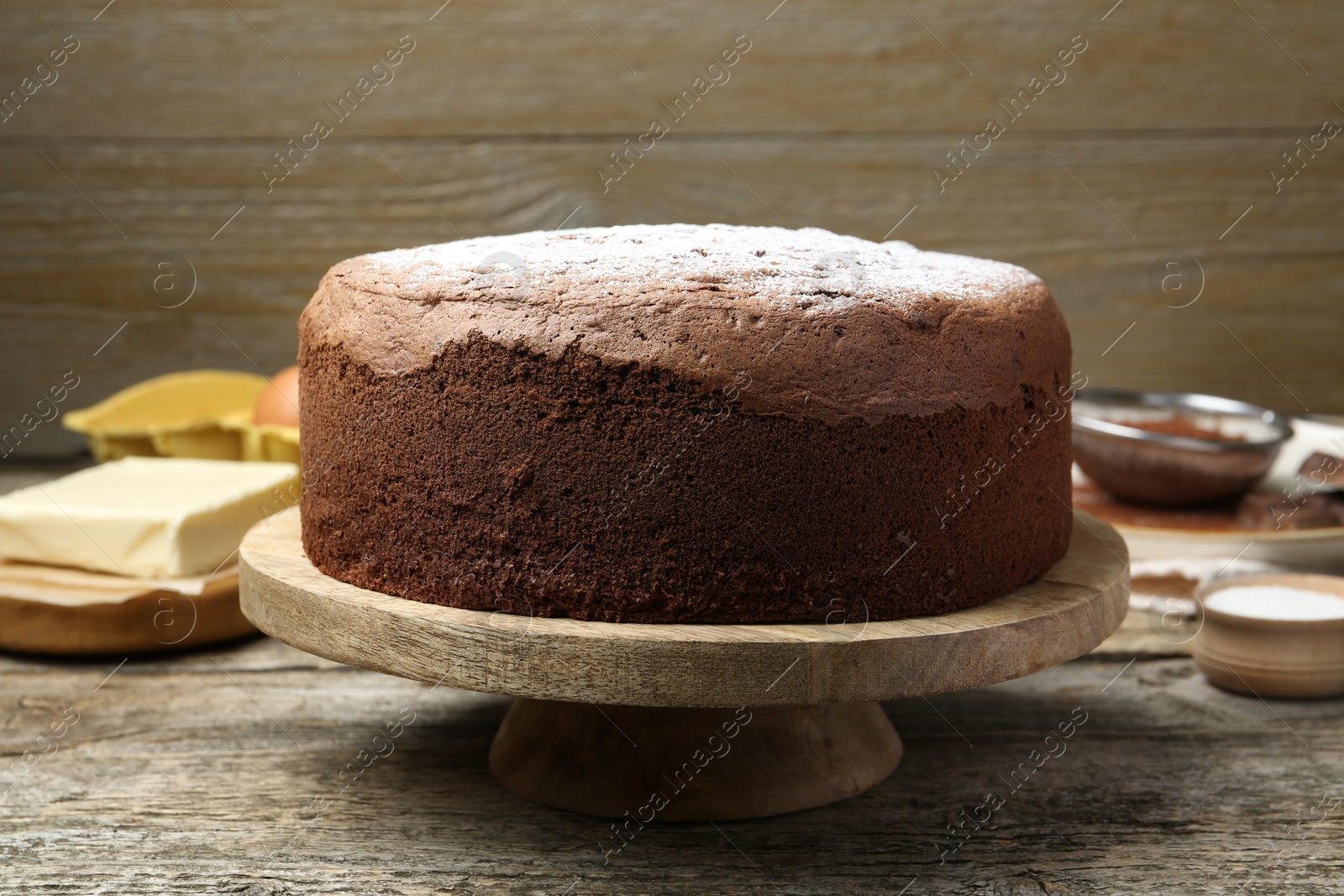 Photo of Tasty chocolate sponge cake with powdered sugar and ingredients on wooden table, closeup