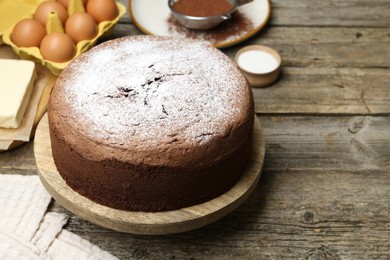 Photo of Tasty chocolate sponge cake with powdered sugar and ingredients on wooden table, closeup