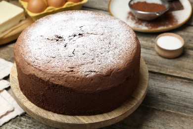 Photo of Tasty chocolate sponge cake with powdered sugar on wooden table