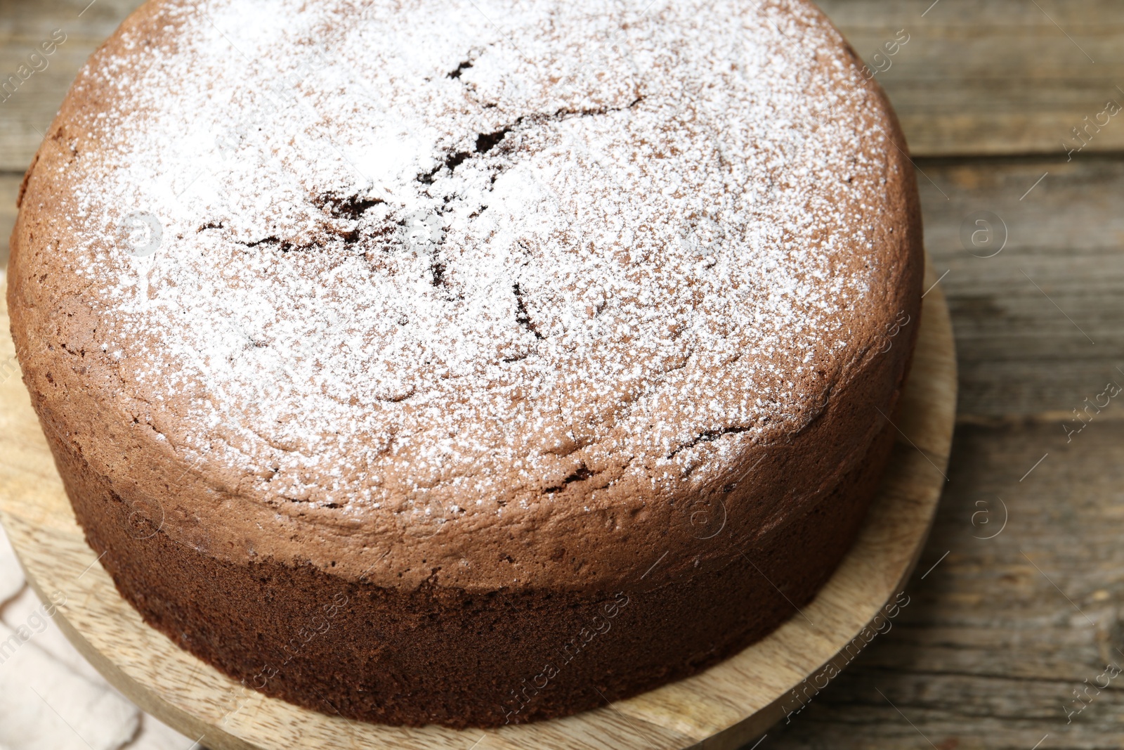 Photo of Tasty chocolate sponge cake with powdered sugar on wooden table, closeup