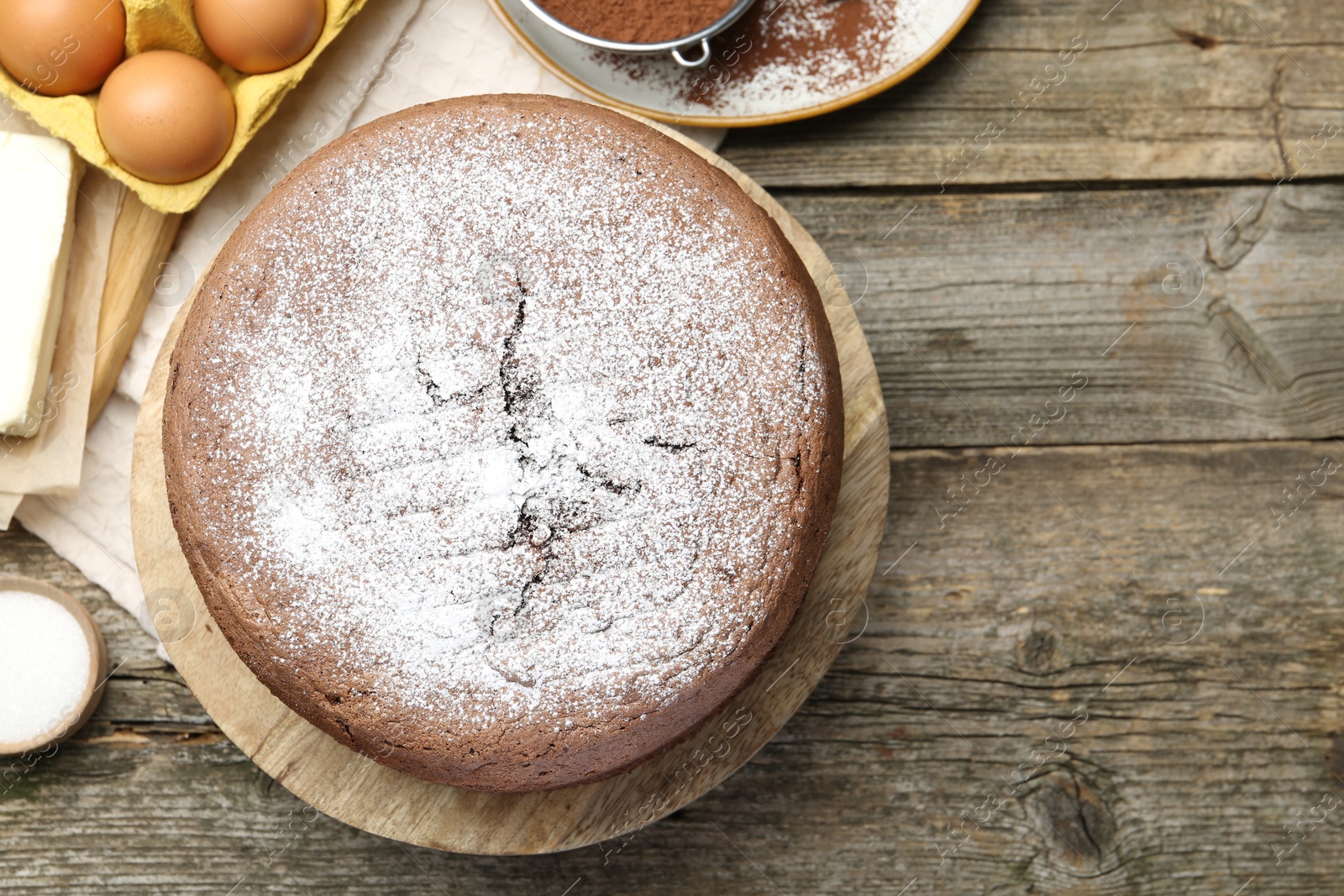 Photo of Tasty chocolate sponge cake with powdered sugar and ingredients on wooden table, flat lay. Space for text