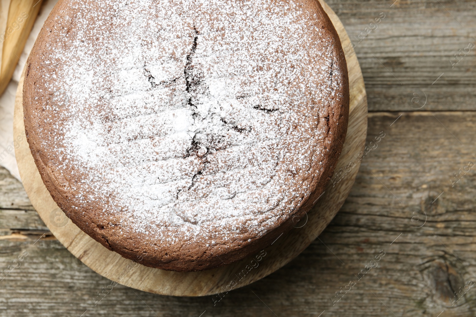 Photo of Tasty chocolate sponge cake with powdered sugar on wooden table, top view