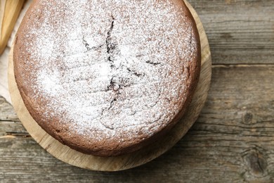 Photo of Tasty chocolate sponge cake with powdered sugar on wooden table, top view