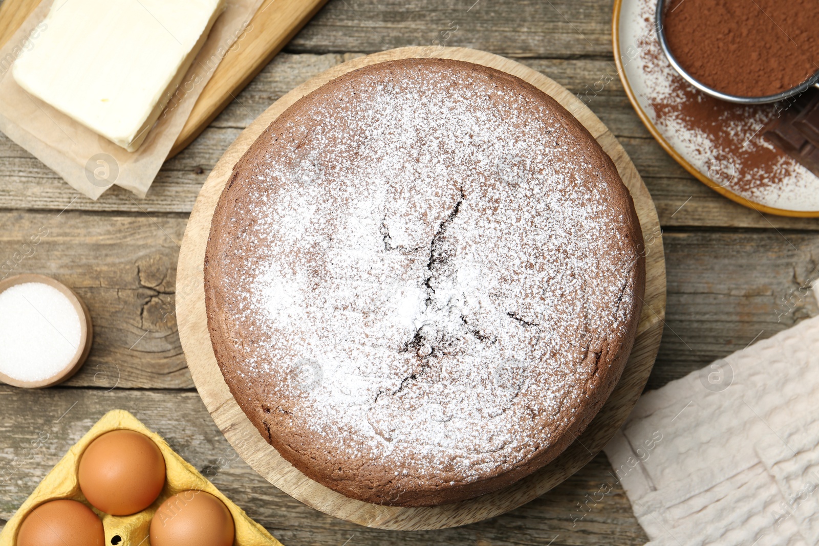 Photo of Tasty chocolate sponge cake with powdered sugar and ingredients on wooden table, flat lay