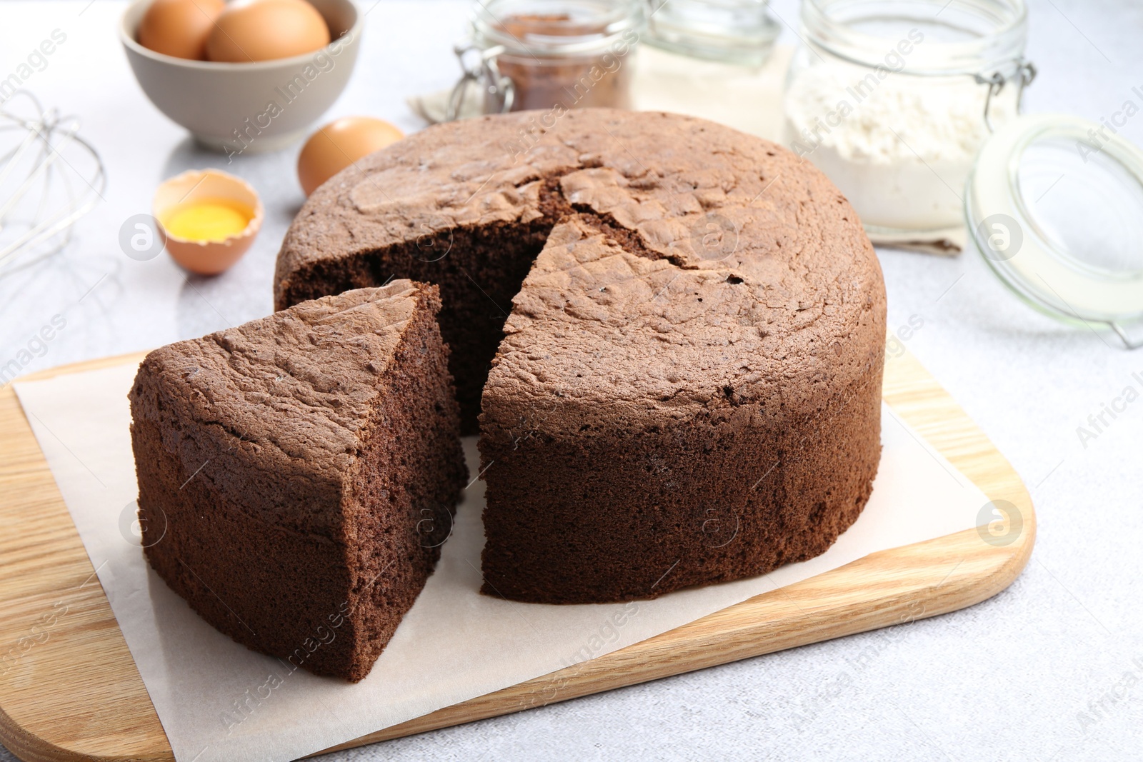 Photo of Cut chocolate sponge cake and ingredients on light table, closeup