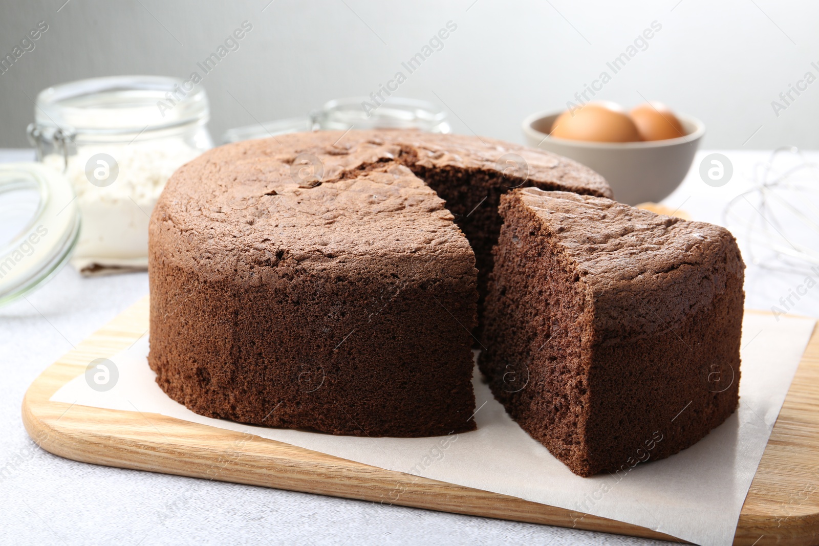 Photo of Cut chocolate sponge cake and ingredients on light table, closeup