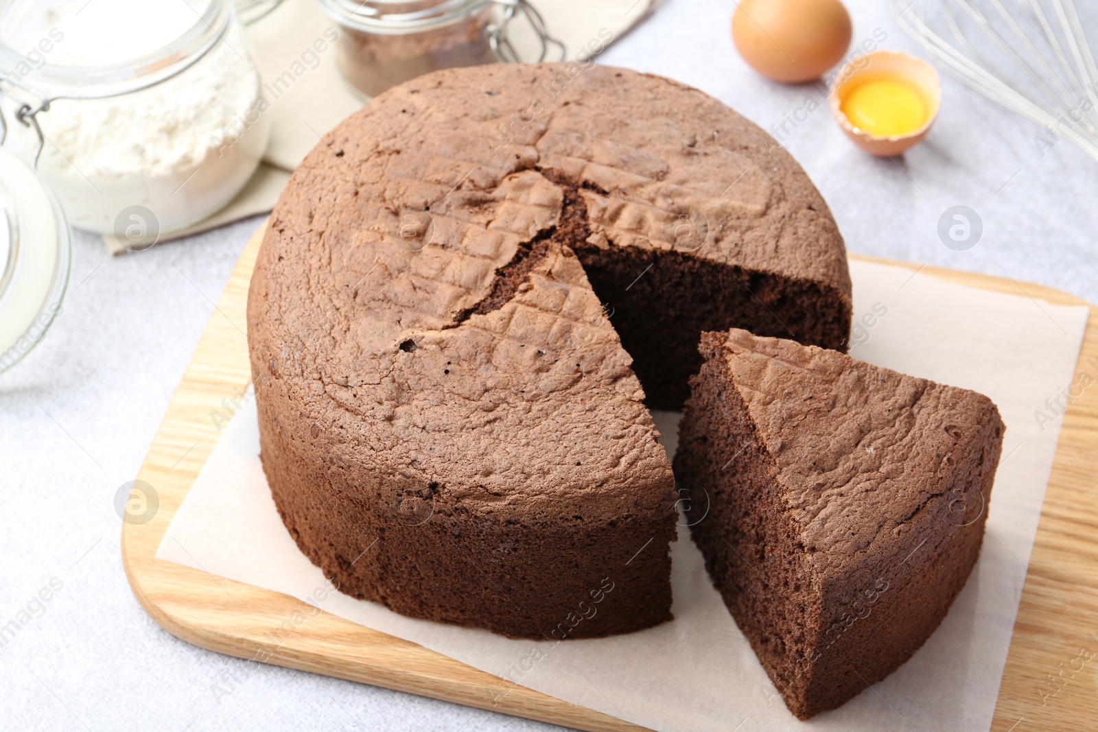 Photo of Cut chocolate sponge cake and ingredients on light table, closeup