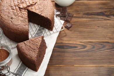 Photo of Cut chocolate sponge cake on wooden table. Space for text