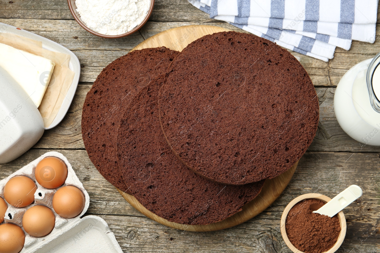 Photo of Cut chocolate sponge cake and ingredients on wooden table, flat lay