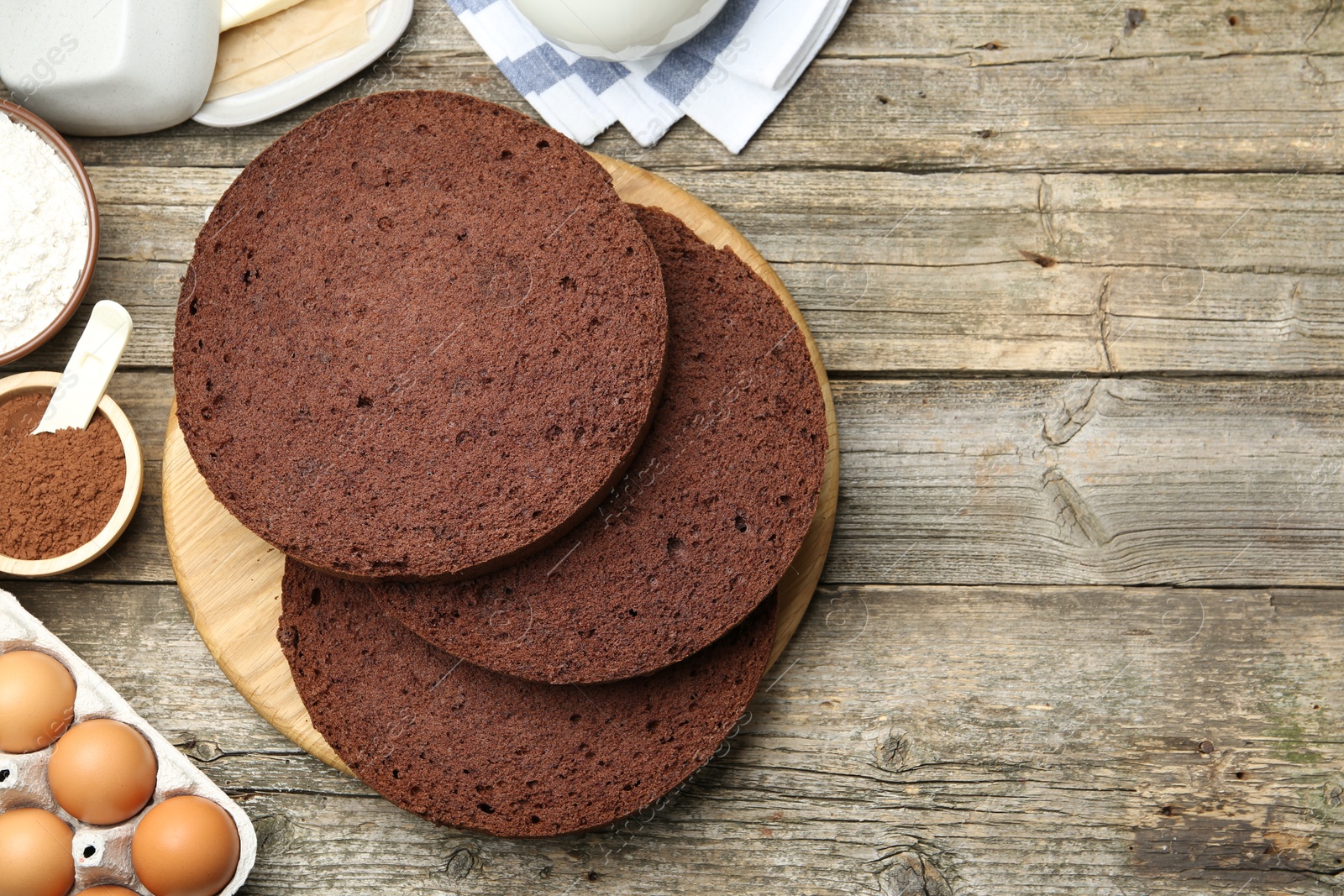 Photo of Cut chocolate sponge cake and ingredients on wooden table, flat lay. Space for text