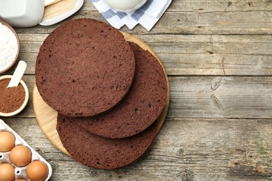 Photo of Cut chocolate sponge cake and ingredients on wooden table, flat lay. Space for text