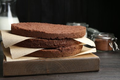 Photo of Cut chocolate sponge cake and ingredients on wooden table, closeup