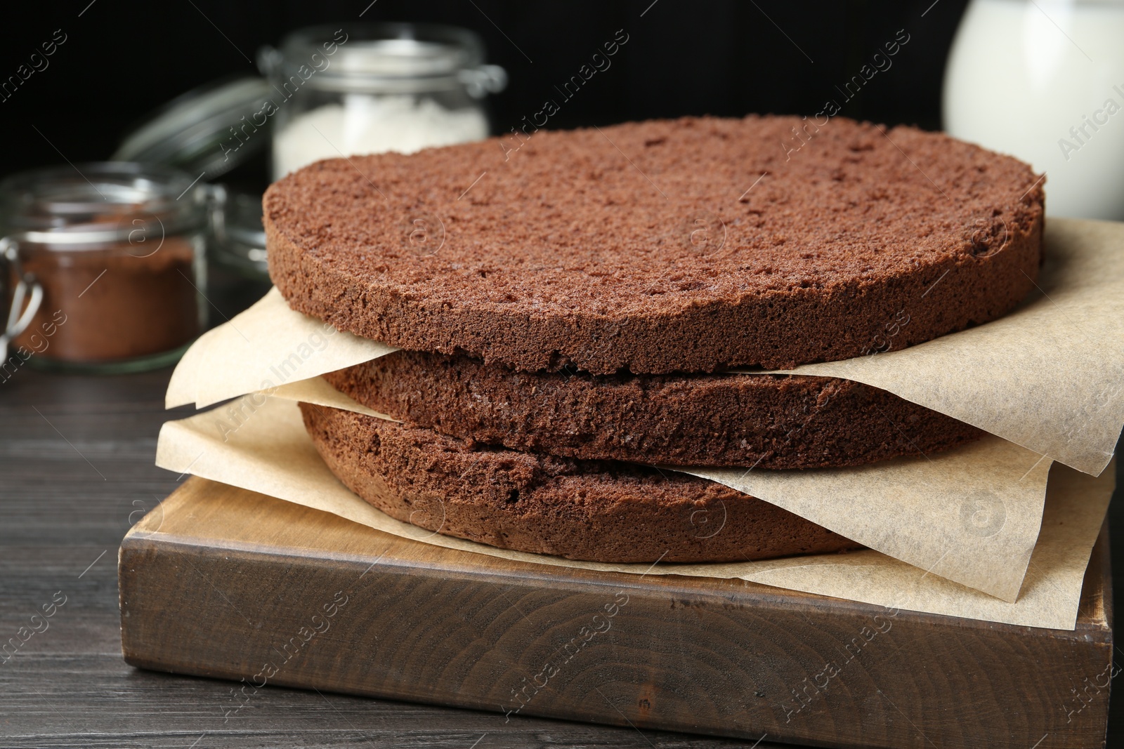 Photo of Cut chocolate sponge cake and ingredients on wooden table, closeup