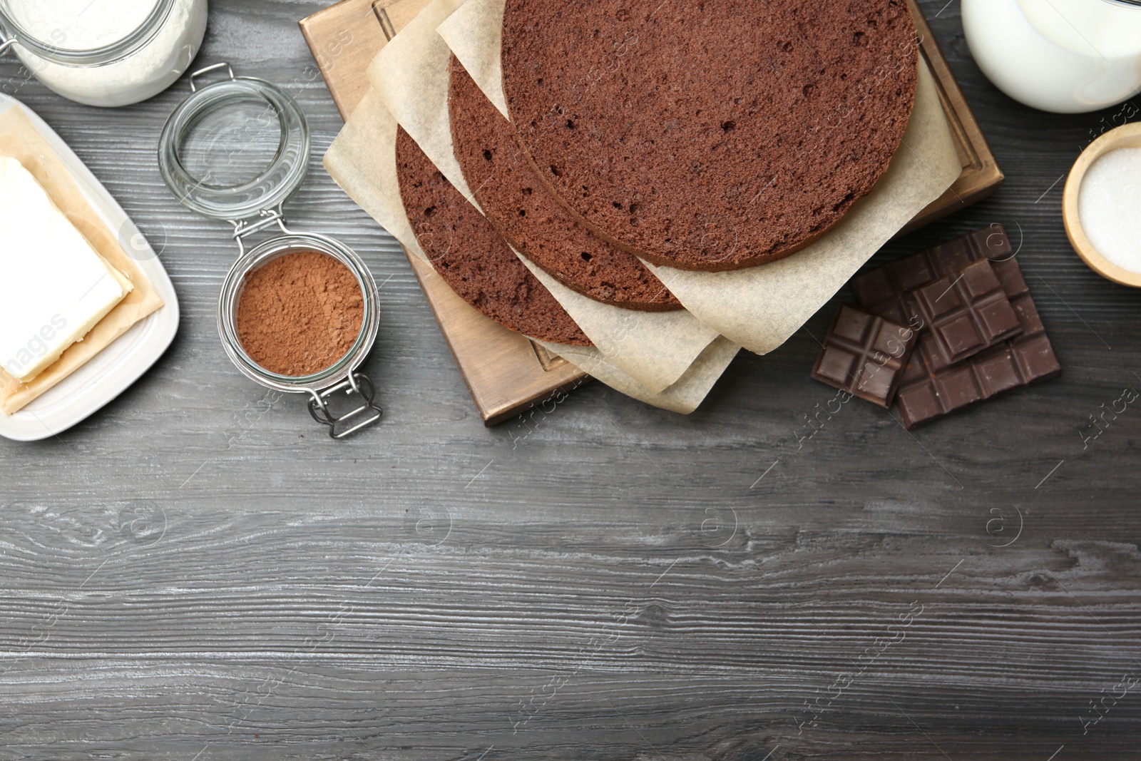 Photo of Cut chocolate sponge cake and ingredients on wooden table, flat lay. Space for text