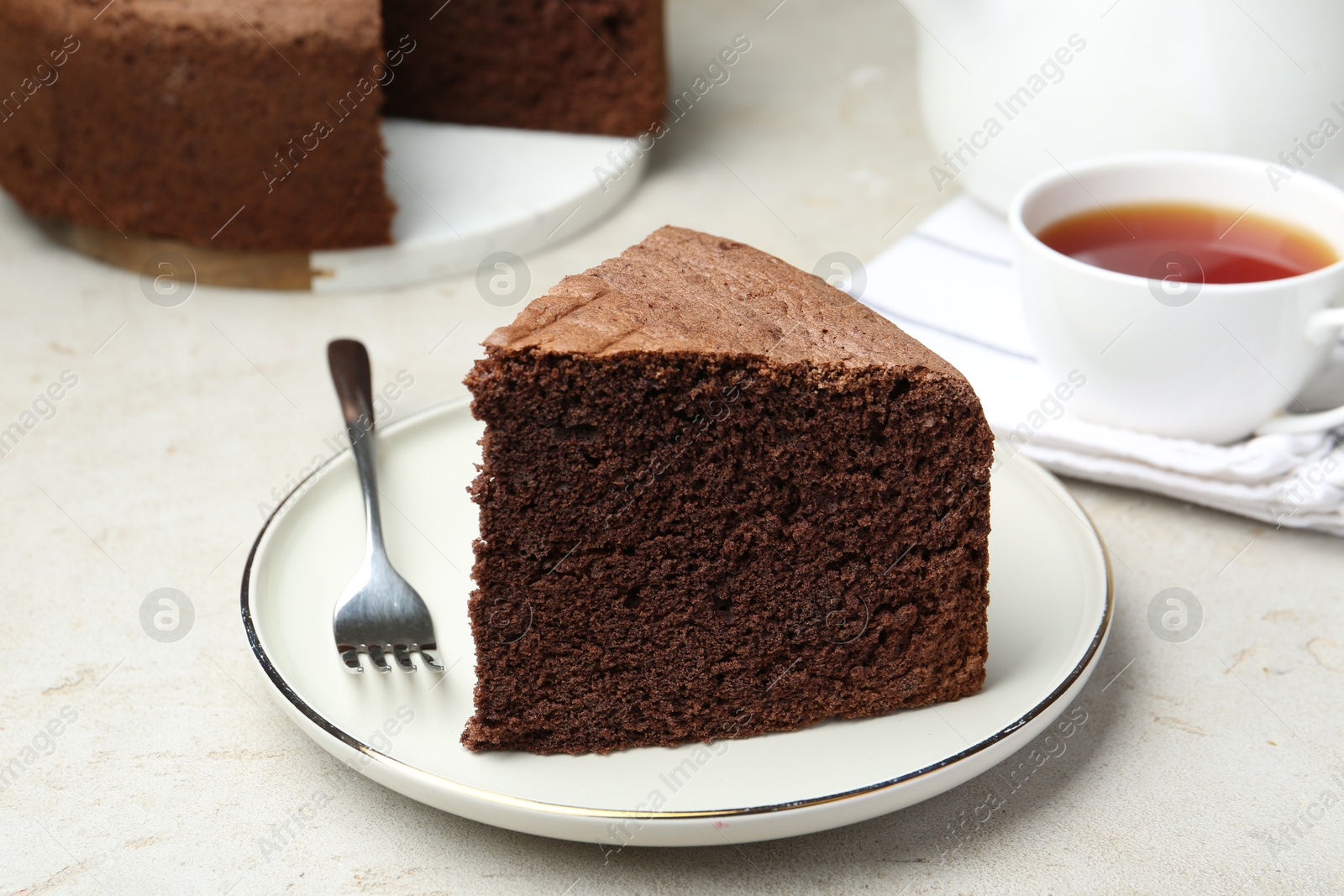 Photo of Piece of tasty chocolate sponge cake served on light table, closeup