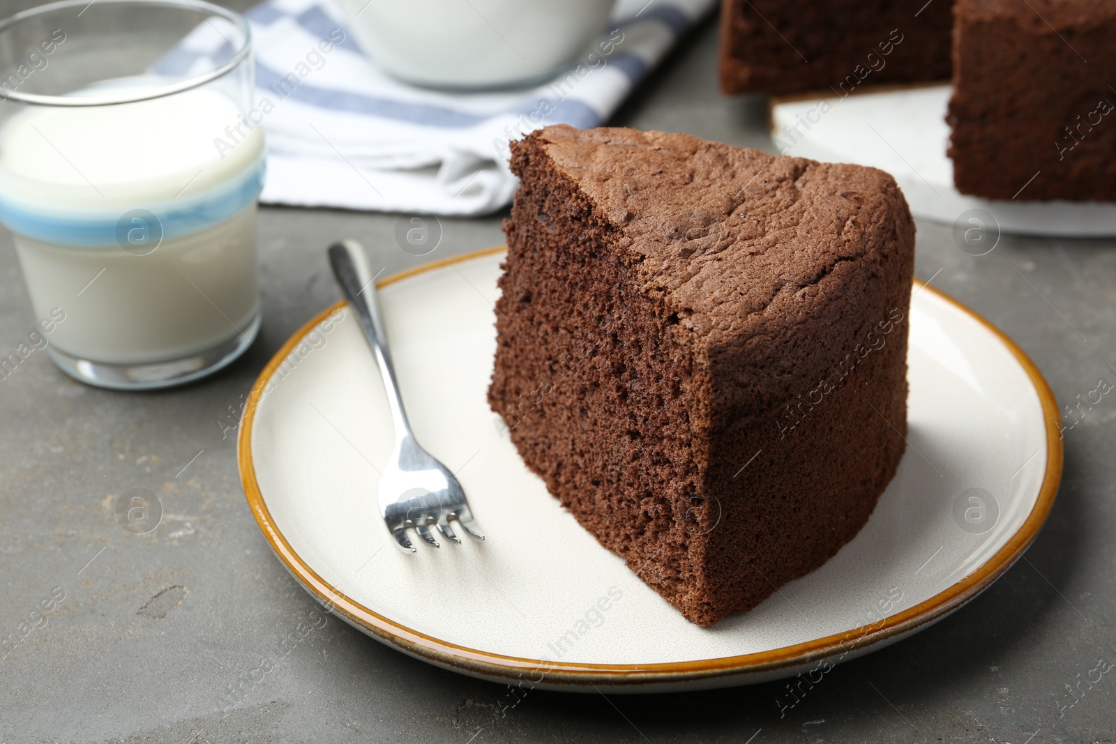 Photo of Piece of tasty chocolate sponge cake served on grey table, closeup