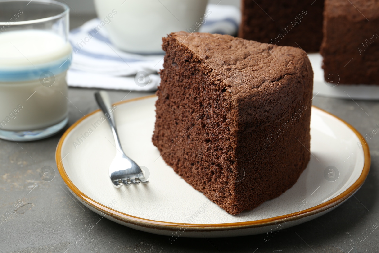 Photo of Piece of tasty chocolate sponge cake served on grey table, closeup