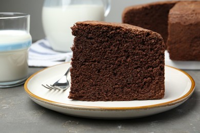 Photo of Piece of tasty chocolate sponge cake served on grey table, closeup