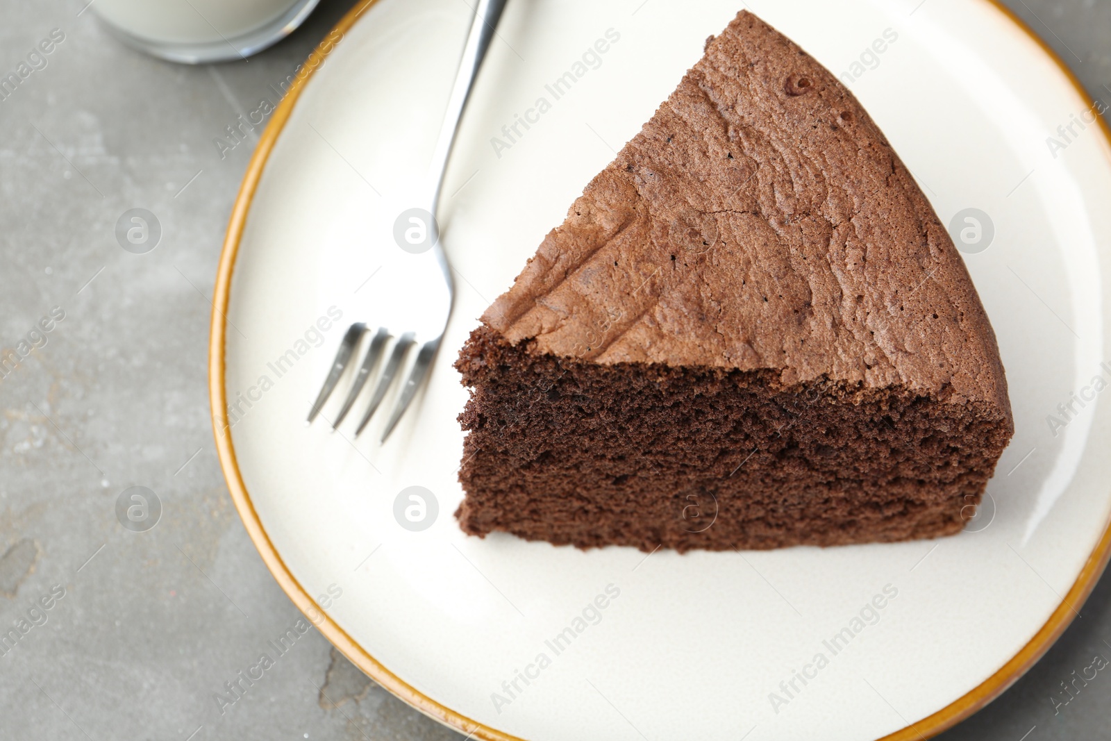 Photo of Piece of tasty chocolate sponge cake served on grey table, closeup